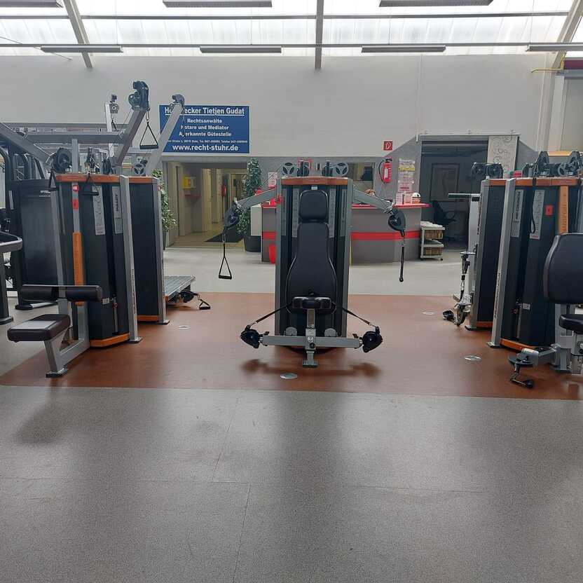 Leere Fitnessstudio-Anlage mit mehreren Krafttrainingsger&auml;ten und einer hellen, gut beleuchteten Umgebung.