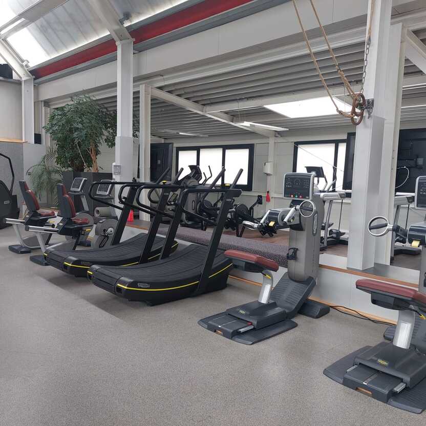 Fitnessraum mit mehreren modernen Trainingsger&auml;ten, darunter Laufb&auml;nder und Ergometer, in heller Umgebung.