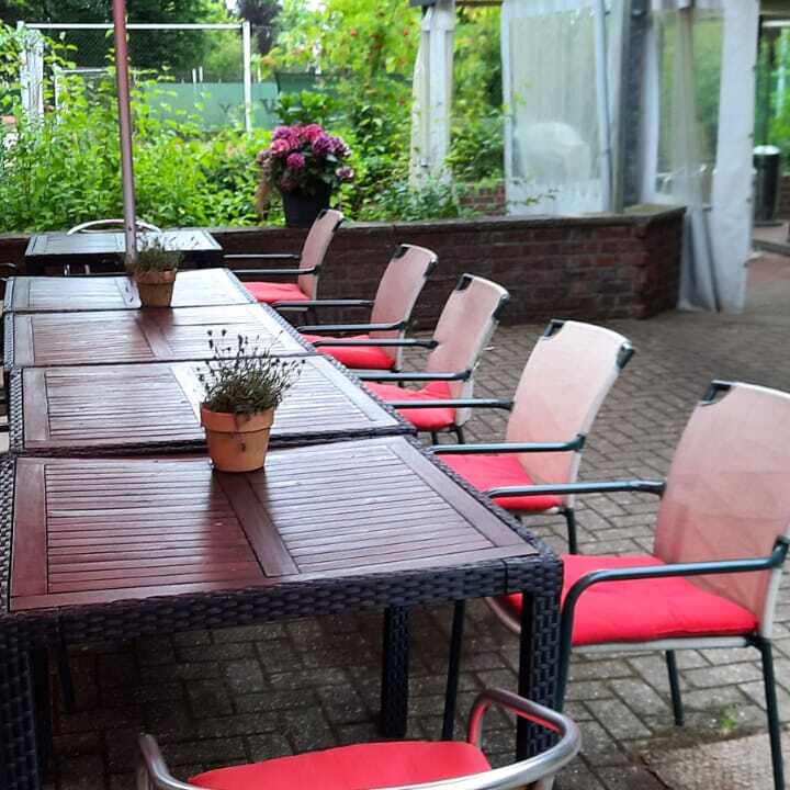 Tisch mit St&uuml;hlen und einem bl&uuml;henden Topf im Freien, &uuml;berdacht von einem roten Sonnenschirm.