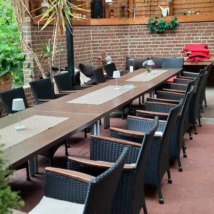 &Uuml;berdachter Essbereich mit langen Holztisch, schwarzen St&uuml;hlen und Pflanzen im Hintergrund. Rustikale Atmosph&auml;re.