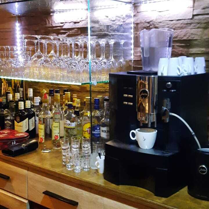 Barbereich mit Gl&auml;sern, Spirituosen und einer Kaffeemaschine auf einer Holzoberfl&auml;che. Beleuchtung hinter Gl&auml;sern.