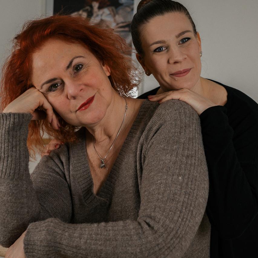 Zwei Frauen posieren l&auml;chelnd in einem Tanzstudio an einer Ballettstange, eine hinter der anderen.