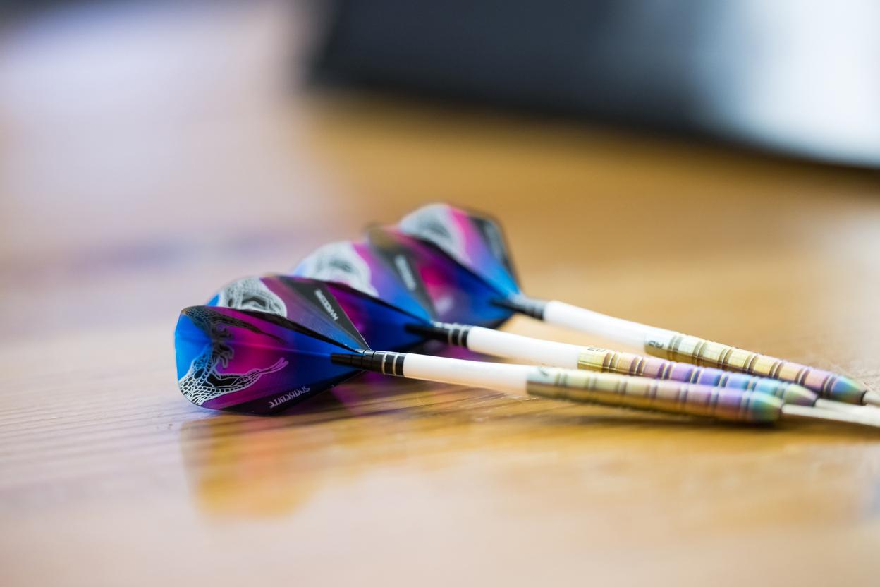 Nahaufnahme von drei Darts mit bunten Flugfedern auf einem Holztisch.