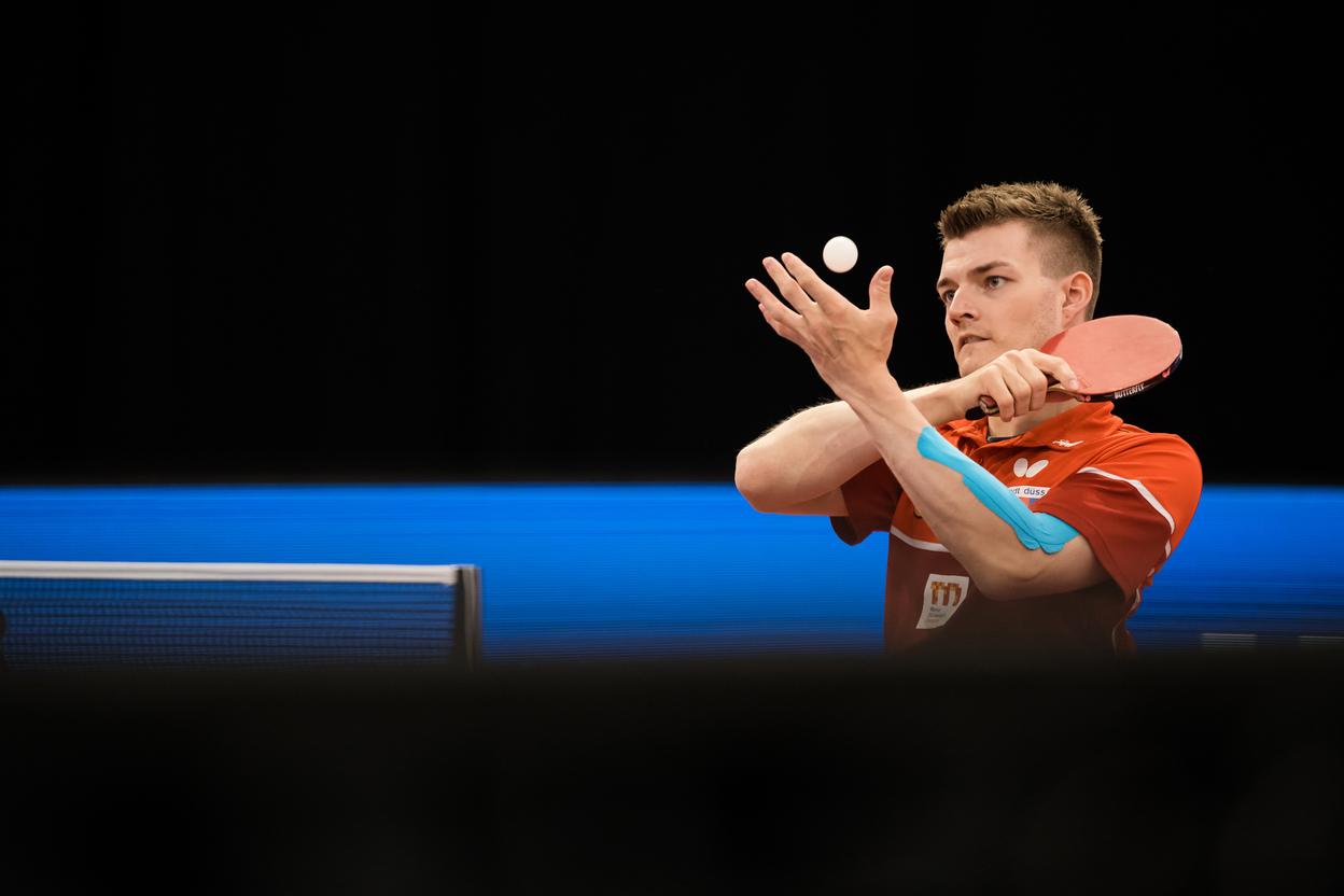 Tischtennisspieler in Aktion, hebt den Ball mit der linken Hand, w&auml;hrend er den Schl&auml;ger in der rechten h&auml;lt.