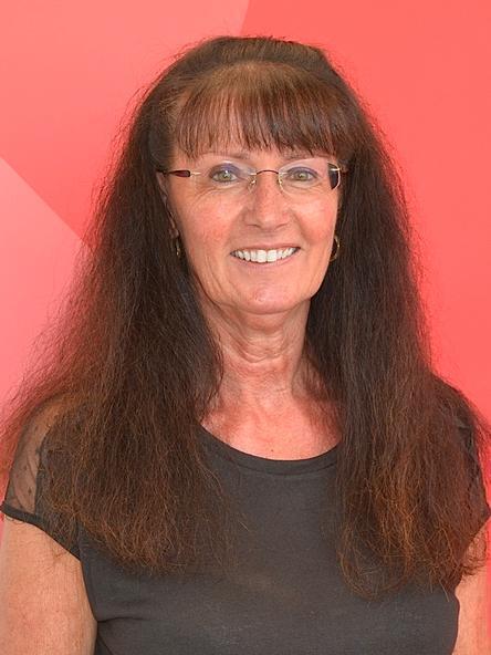 Portr&auml;t einer l&auml;chelnden Frau mit langen, dunklen Haaren und Brille vor einem roten Hintergrund.