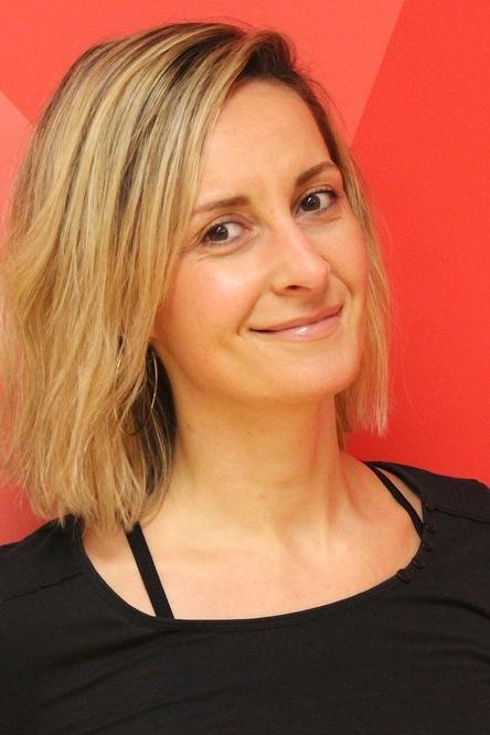 Portrait einer l&auml;chelnden Frau mit schulterlangen, blonden Haaren vor einem roten Hintergrund.