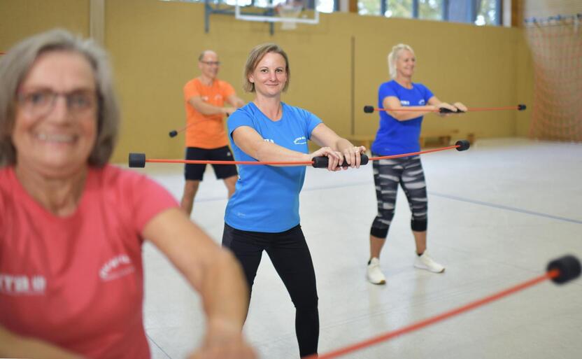 Gruppentraining mit vier Personen, die mit Widerstandsband in einem Sportraum &Uuml;bungen durchf&uuml;hren.