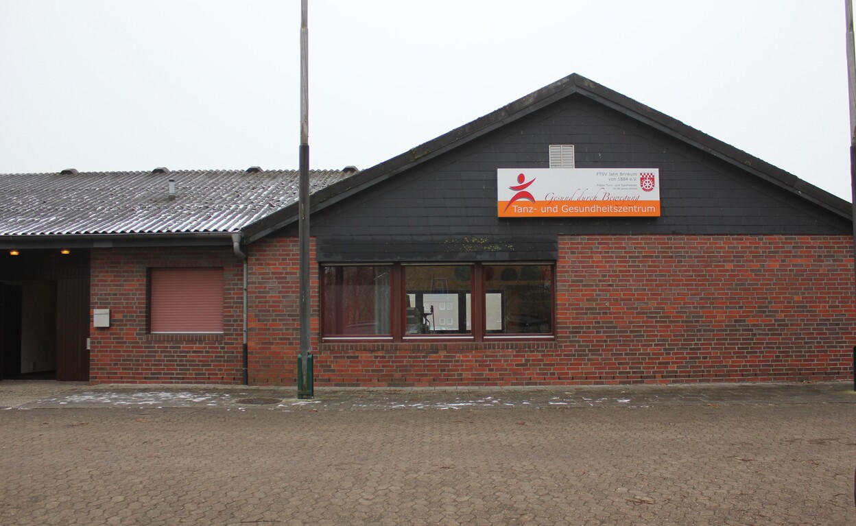 Geb&auml;udeansicht eines Gesundheitszentrums mit rot-orangefarbener Ziegelwand und einem wei&szlig;en Schild an der Fassade.
