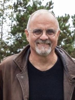 Mann mit Brille und kurzer Haarfrisur steht l&auml;chelnd neben einem Holzst&uuml;ck mit der Aufschrift &bdquo;50 Jahre&ldquo;.