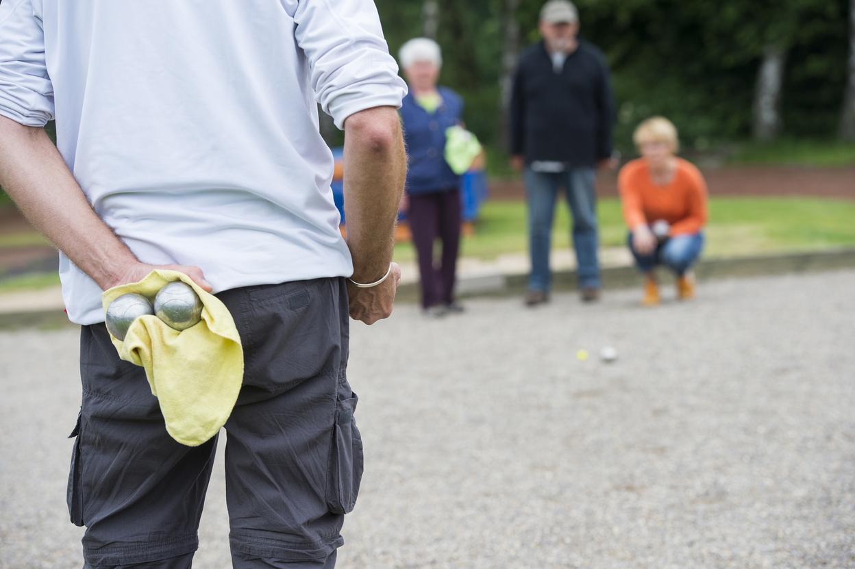Person hält zwei Metallkugeln in einem gelben Handtuch, während andere Personen im Hintergrund zuschauen.