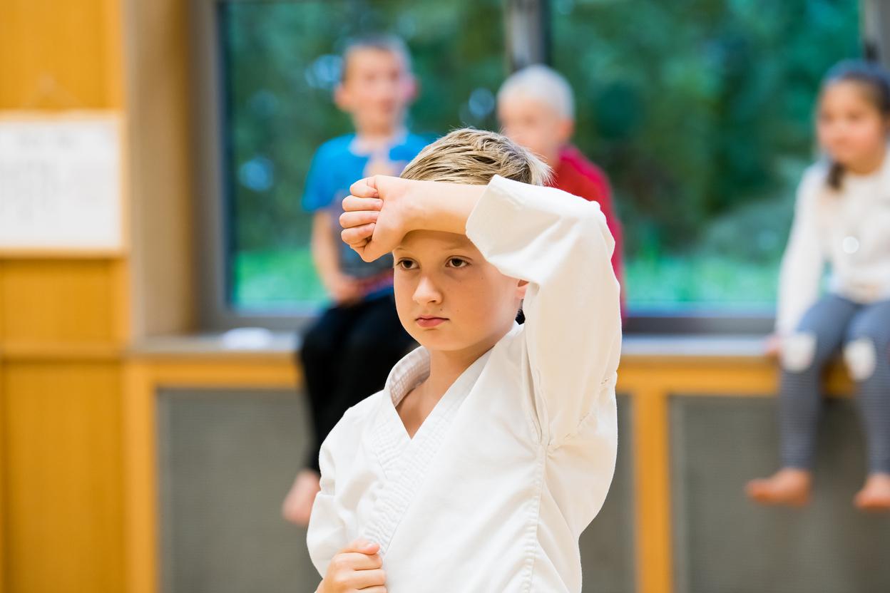 Junge in Karate-Uniform mit ernstem Gesichtsausdruck, während er eine Übung vor einer Fensterfront ausführt.